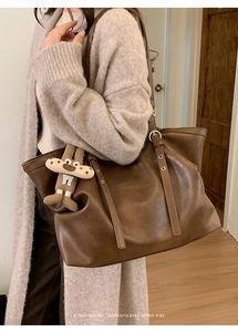 Detail of dark brown leather tote bag with metal buckle and cute cartoon pendant charm
