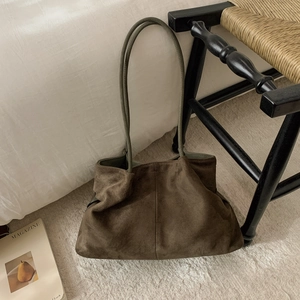 Detail of a large dark brown suede tote bag with slim green straps in a cozy room setting