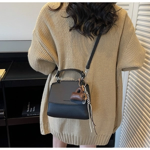 Black pebbled leather tote bag with brown charm accessory worn by model in beige sweater