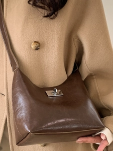 Brown vintage faux leather crossbody bag with silver clasp worn on a khaki coat