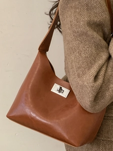 Minimalist brown leather crescent shoulder bag with silver clasp worn on a wool blazer