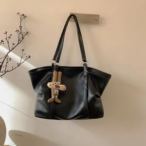 Detailed close-up of a black leather tote bag with a cute brown plush animal pendant charm