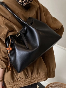 Grand sac cabas noir en cuir avec pendentif en bois vintage porté sur un manteau marron