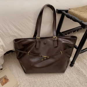 Macro detail of dark brown tote bag showing smooth leather texture and gold metal hook