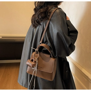 Detailed side view of brown lychee grain leather tote bag with mini bag charm and strap