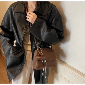 Close-up of brown leather crossbody bag featuring lychee texture and logo pendant detail