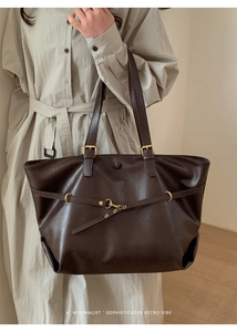 Detailed view of deep brown matte leather tote bag featuring gold metal hardware on model