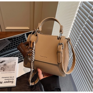 Close-up of litchi grain leather handbag with metal buckle and mini bag charm