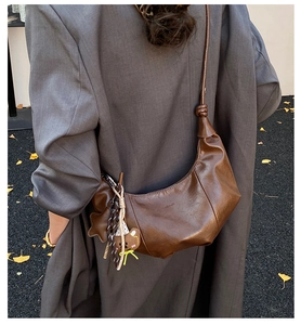 Nahaufnahme braune Leder-Tasche mit Stern- und Bärenanhänger auf grauem Blazer