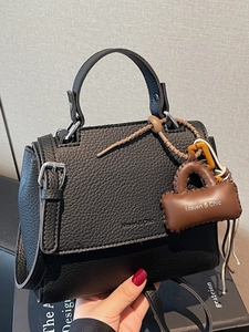 Elegant black lychee leather handbag with a top handle and a brown charm accessory
