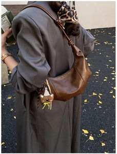 Nahaufnahme der braunen Halbmond-Achseltasche mit Ledertextur und Bärenanhänger