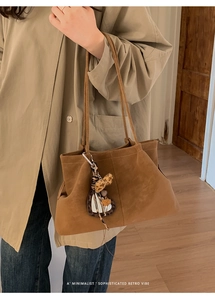 Close-up of brown suede tote bag with leopard heart charm on a trench coat model