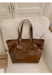 Detail view of brown vintage leather tote bag on white sofa with minimalist metal buckle