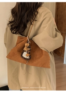Close-up of a brown suede tote bag with leopard print bear charm on a female model
