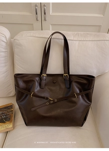 Detail of a deep brown faux leather tote bag with glossy texture on a white sofa