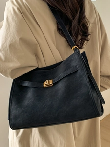Minimalist navy blue tote bag with gold swivel lock shown on model with trench coat