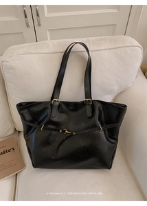 Detail view of black vintage leather tote bag with gold hardware on a white sofa
