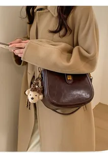 Detail of dark brown vintage saddle bag featuring a gold buckle and bear plush charm