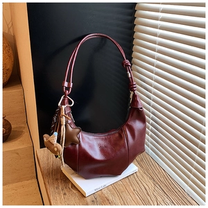 Detailansicht der weinroten Hobo-Tasche aus Leder mit Bären-Anhänger bei sanftem Licht