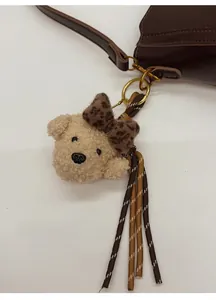 Close-up of white plush bear charm with leopard bow and tassel on leather bucket bag