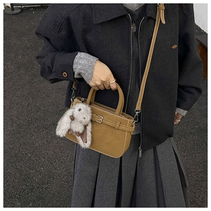 Close-up of vintage brown leather handbag with decorative buckle and plush rabbit charm