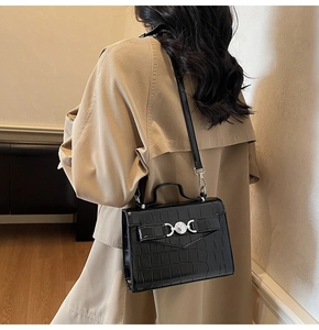 Détail du sac à main noir texture crocodile avec boucle argentée sur fond manteau camel
