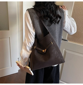 Detail view of coffee leather bucket bag with gold metal buckle on a model in retro style