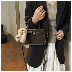 Detail view of dark brown vintage handbag featuring a buckle design and plush rabbit charm