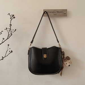 Detail of black semi-circular bucket bag with golden buckle and plush puppy charm