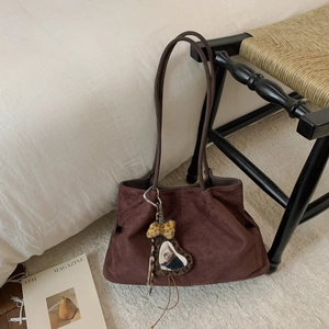 Detail of a dark brown suede tote bag with leopard and plush heart charms in home setting