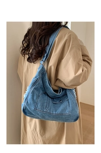 Detail of vintage blue denim shoulder bag with functional pockets and frayed fringe accents