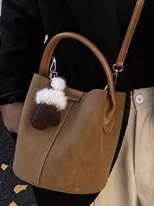 Borsa a secchiello in pelle marrone con ciondolo di peluche, indossata da modella in cappotto