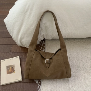 Detailed view of brown faux suede shoulder bag with silver metal buckle in a cozy setting