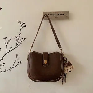 Detail view of brown retro bucket bag with gold square buckle and plush bear charm