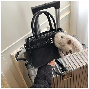 Detail of black matte handbag with contrast stitching and fluffy rabbit charm on luggage