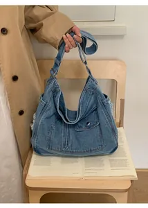 Detail of blue washed denim tote bag with frayed edges and wide shoulder strap