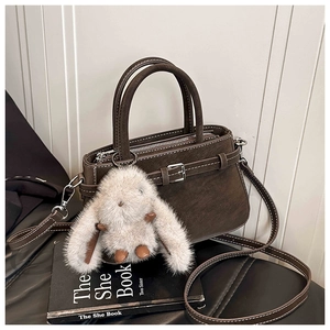 Detail of dark brown vintage handbag with plush bunny charm on black leather and books