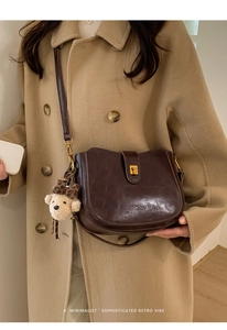 Detail of dark brown leather bucket bag with metallic lock and cute plush bear charm