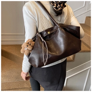 Close-up of a large brown leather tote bag with a cute plush puppy charm on the side