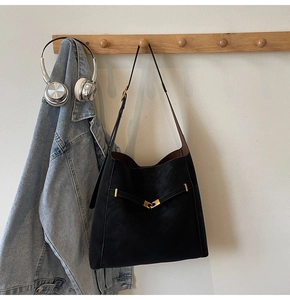 Detail of black suede tote bag hanging on wooden rack with gold metal buckle hardware