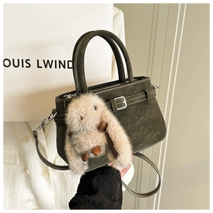 Detail view of vintage olive green leather handbag with a plush bunny charm accessory