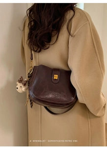 Close-up of retro brown saddle bag with golden buckle and bear charm on wool coat