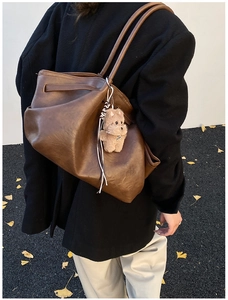 Close-up of brown leather tote bag featuring a cute plush bear pendant and tassel detail