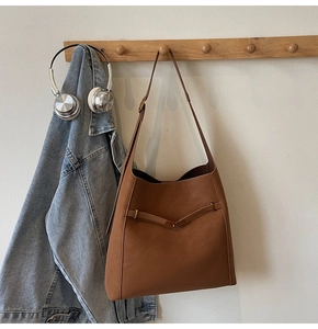 Close-up of brown leather bucket bag with metallic buckle on wooden hanger and denim jacket