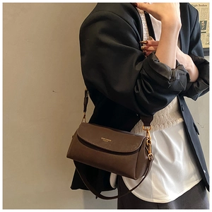 Détail d'un sac bandoulière vintage en cuir marron avec logo doré sur fond beige
