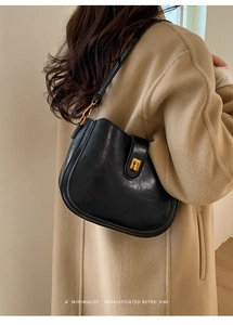 Chic black shiny leather saddle bag with gold buckle detail worn with a wool coat