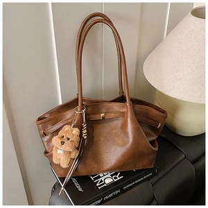 Detail shot of brown vintage leather tote bag with a teddy bear charm on books