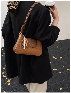 Detail of a brown suede shoulder bag with woven strap and ethnic wooden bead tassels
