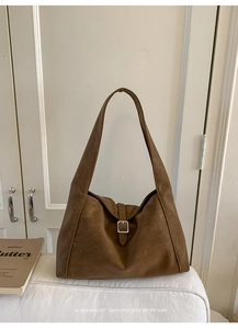 Detail of a large brown tote bag with decorative strap buckle in a minimalist setting