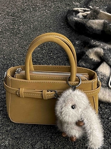 Retro mustard yellow leather handbag with rabbit charm on a minimalist urban background